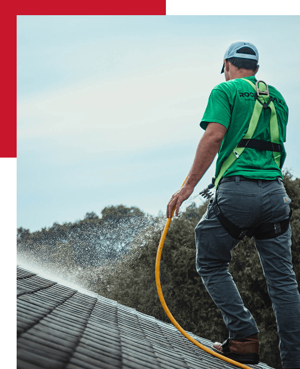 technician in a green shirt spraying a roof with a hose