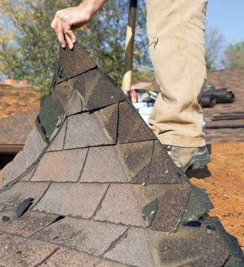 roofer carrying a stack of asphalt shingles across a roof