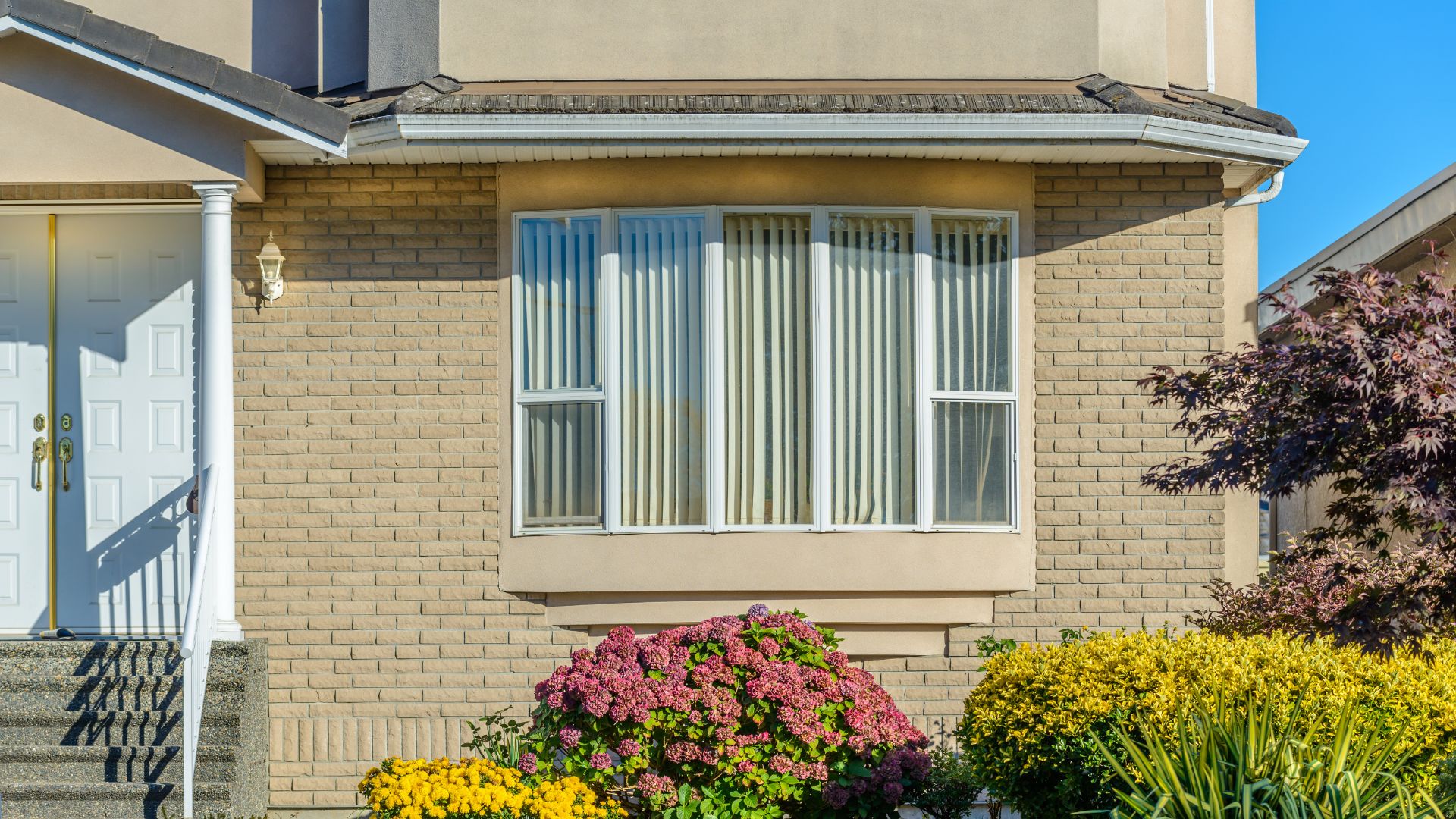 roof-restoration A large, five-pane bay window on the front of a beige brick suburban home.