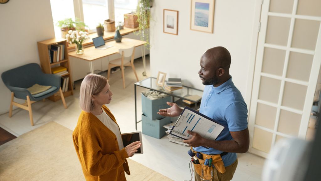 contractor with a clipboard talking to a homeowner in a living room