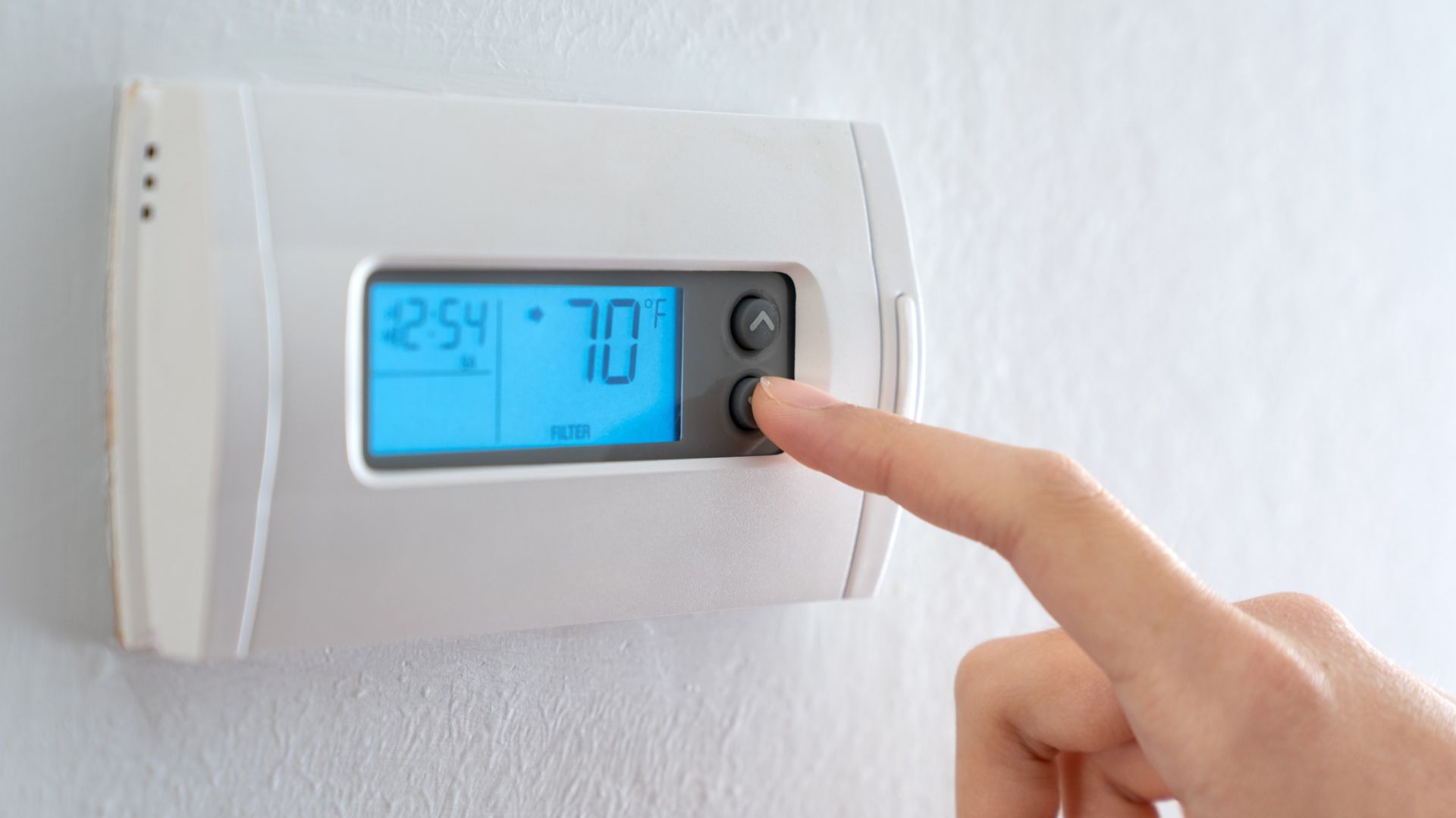 roof-restoration A hand adjusting a wall thermostat that reads 70 degrees F.
