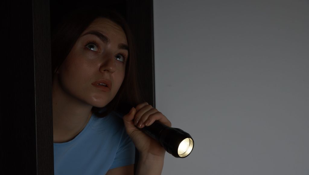 A young homeowner opening a door in her home, holding out a lit flashlight.